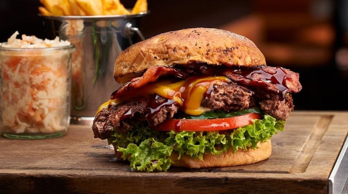 Kahuna Burger mit Bacon, Cheddar und Teriyaki-Sauce, dazu Pommes und Krautsalat auf einem Holzbrett