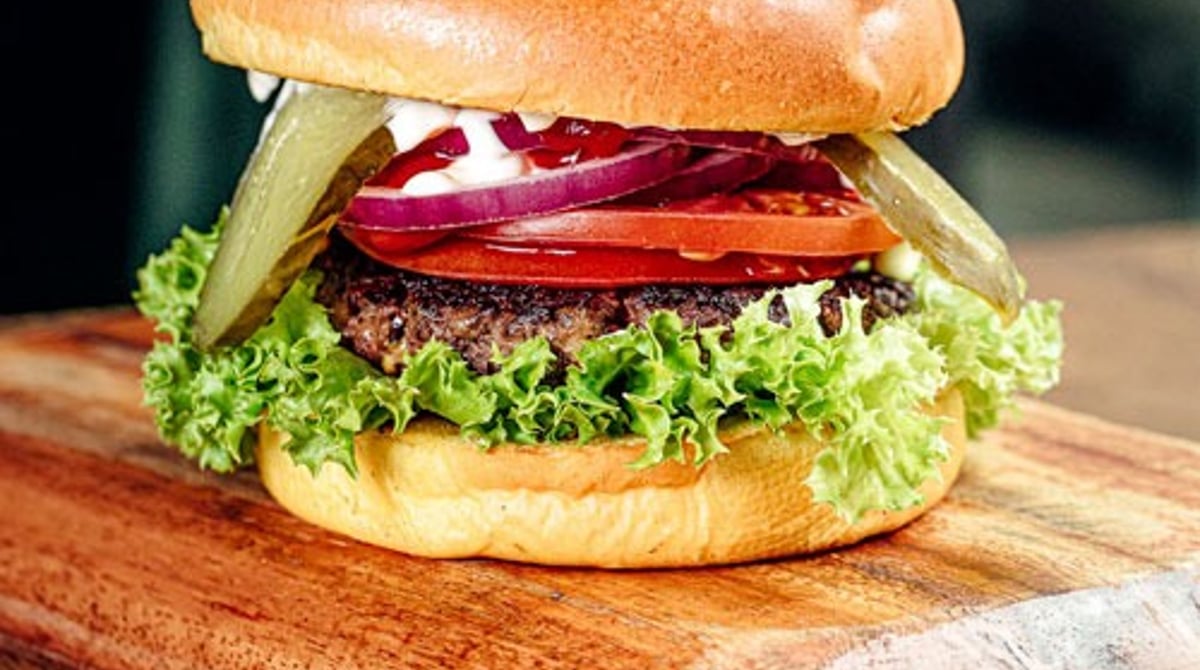 Burger mit Salat, Tomate, roten Zwiebeln und Gewürzgurke auf einem Holzbrett