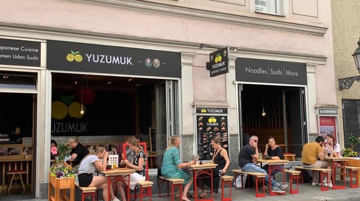 Außenansicht des Yuzumuk an der Westenriederstraße mit Gästen an Bierbänken vor den geöffneten Fensterfronten
