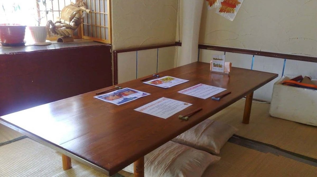 Raum mit niedrigem Holztisch, Sitzkissen und Tatami-Boden im Ohayou