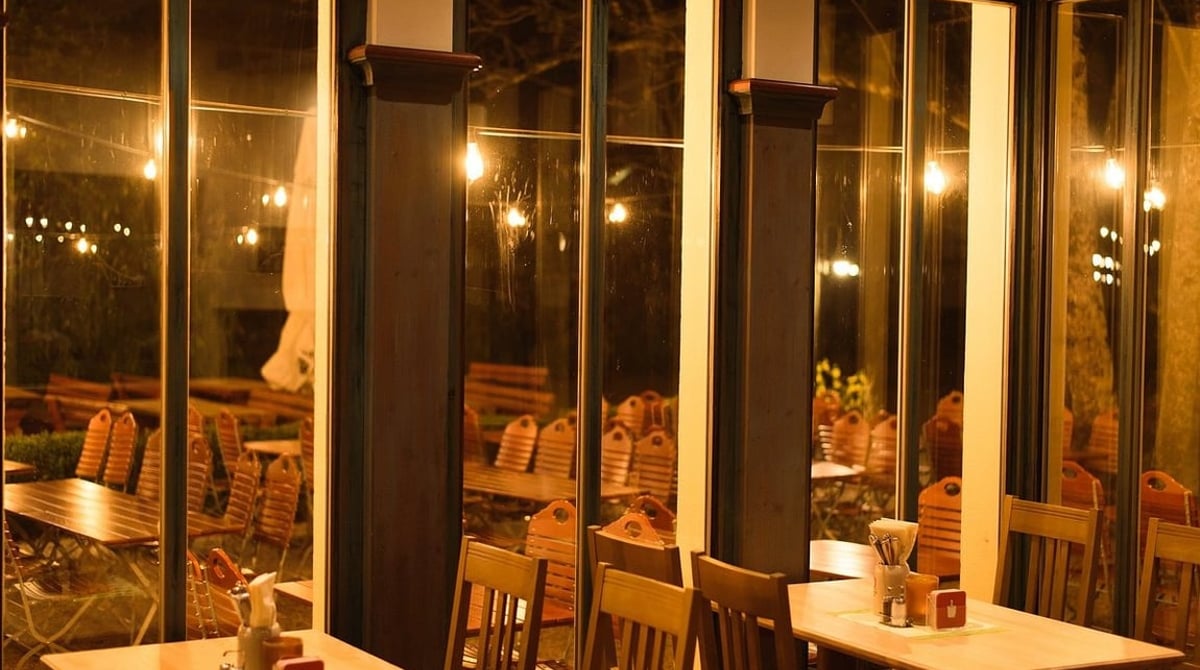 Gastraum mit großen Fenstern und Holztischen am Abend im Gasthaus Maxhof