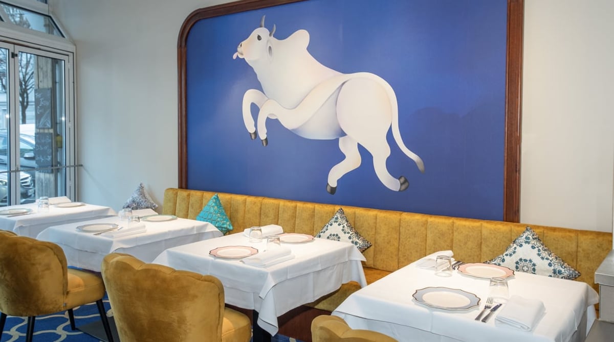 Gastraum des The Indian Room mit weiß eingedeckten Tischen, gelben Sesseln und großem Wandbild eines weißen Stiers