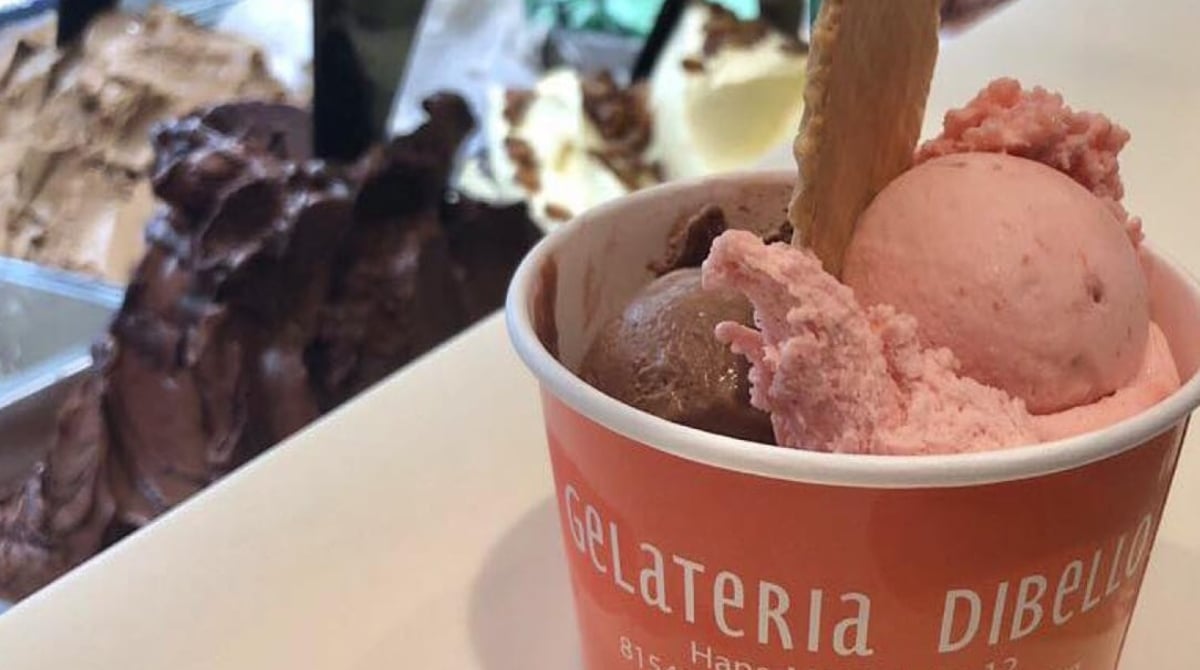 Becher mit Schoko- und Erdbeereis und Waffel vor der Eistheke der Gelateria Dibello
