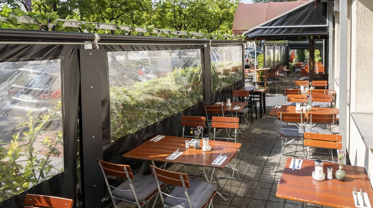 Überdachte Terrasse des KeKo mit Holztischen und roten Stühlen