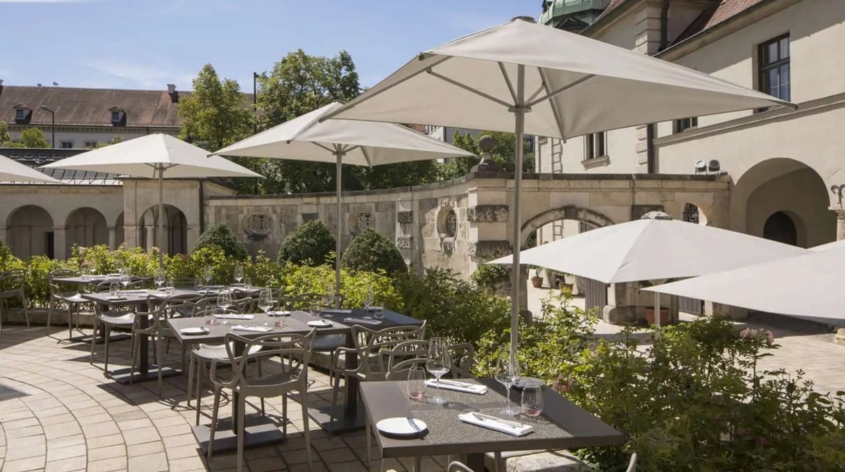 Terrasse des Restaurants Museum mit gedeckten Tischen und weißen Sonnenschirmen vor den Arkaden des Bayerischen Nationalmuseums