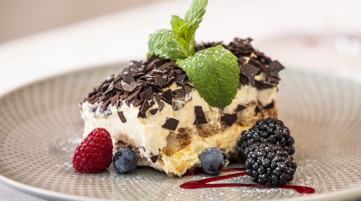 Tiramisu mit Schokoladenspänen, Beeren und Minze auf einem grauen Teller