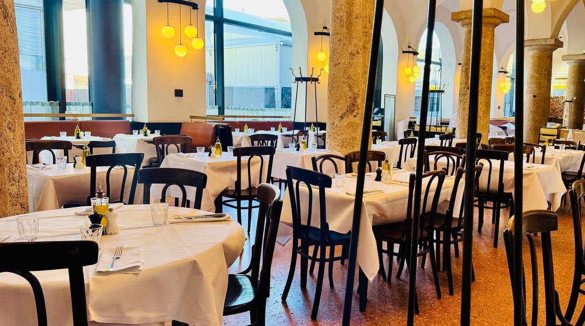 Gastraum des Brenner Grill mit weiß eingedeckten Tischen, Bugholzstühlen, Steinsäulen und gelben Pendelleuchten