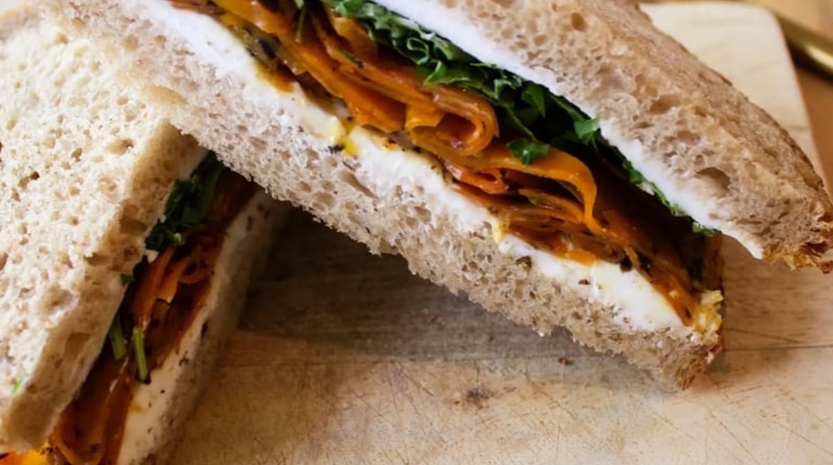 Aufgeschnittenes Sandwich mit Gemüse und Frischkäse auf einem Holzbrett