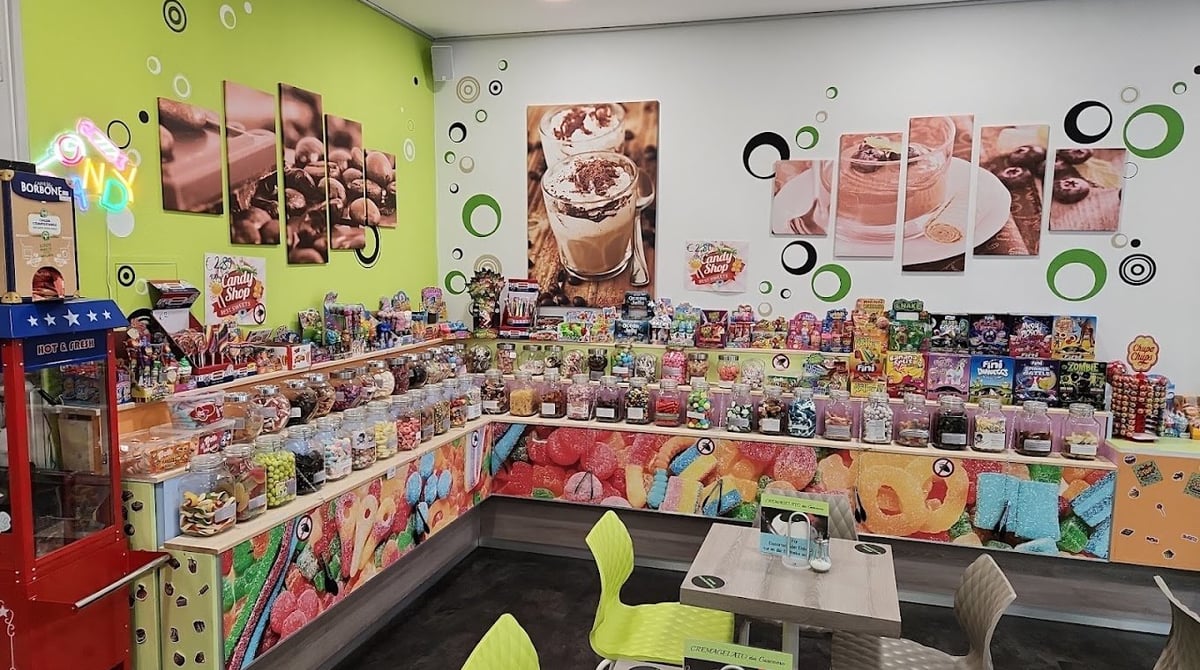 Ecke im Laden mit Regalen voller Bonbongläser, Fruchtgummi und einem Tisch mit Stühlen