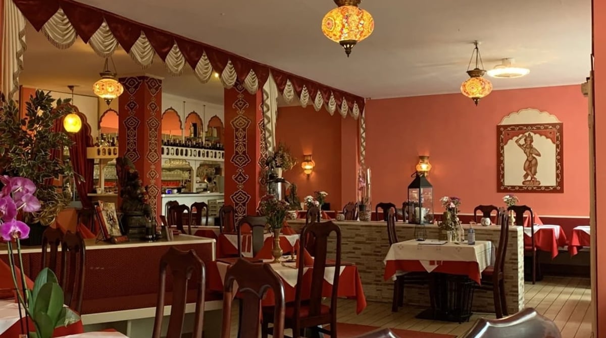 Gastraum des Ganga in München mit lachsroten Wänden, Orientlampe, gedeckten Tischen und Blumen