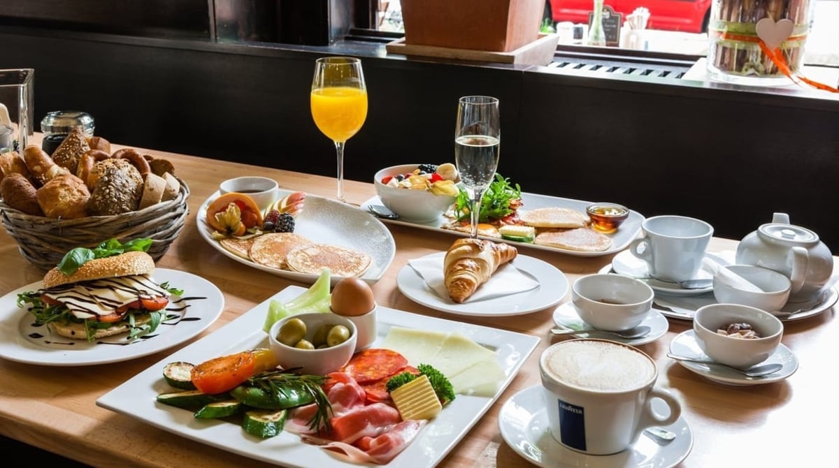 Frühstücksteller mit Brötchen, Croissant, Aufschnitt, Orangensaft und Cappuccino