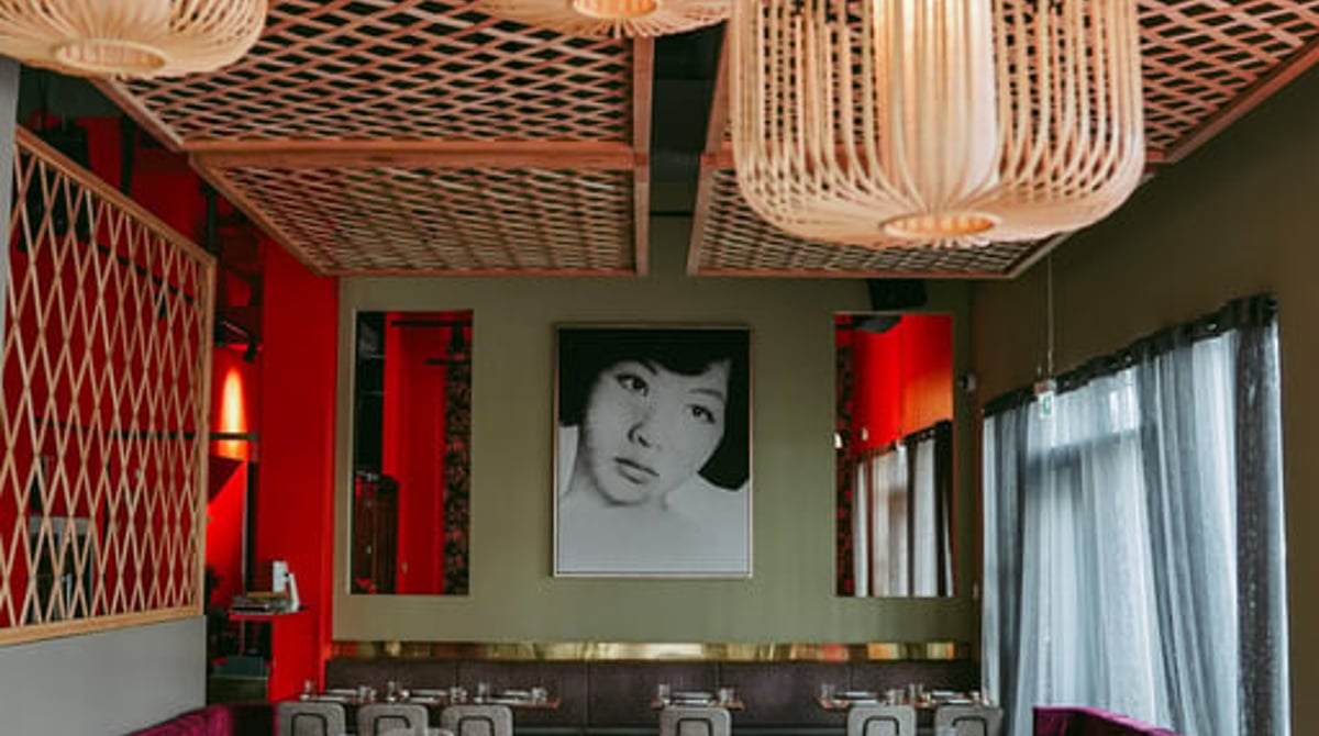 Gastraum des Jaadin Grillhouse mit Bambus-Lampen, Samtbänken und dem Porträt einer jungen Frau an der Wand