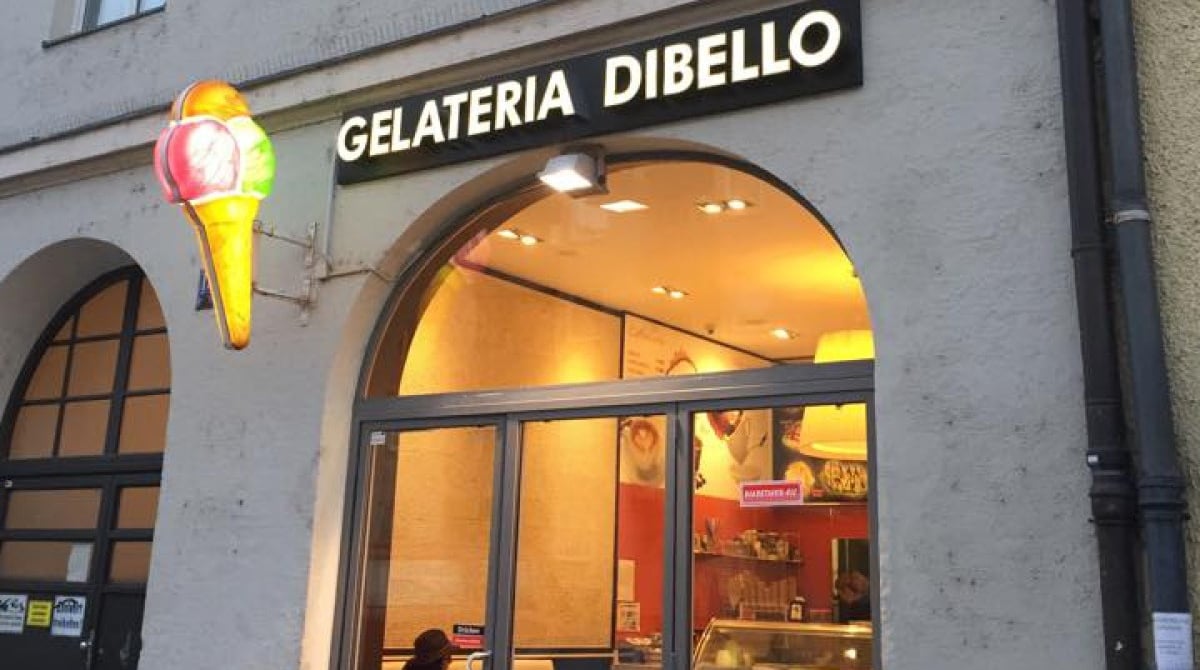 Abendlich beleuchteter Eingang der Gelateria Dibello mit Leuchtschrift und Eiswaffel