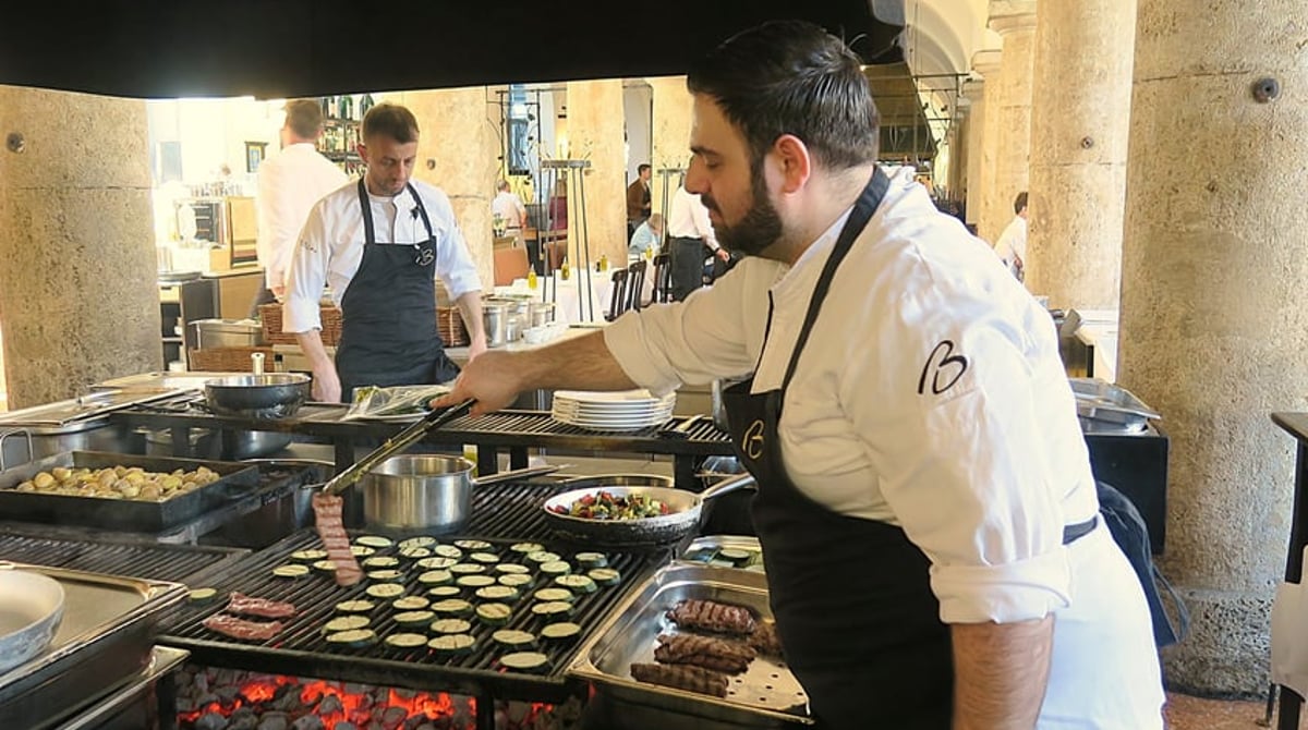 Koch an der offenen Feuerstelle des Brenner mit Gemüse, Spießen und Pfannen auf dem Grillrost