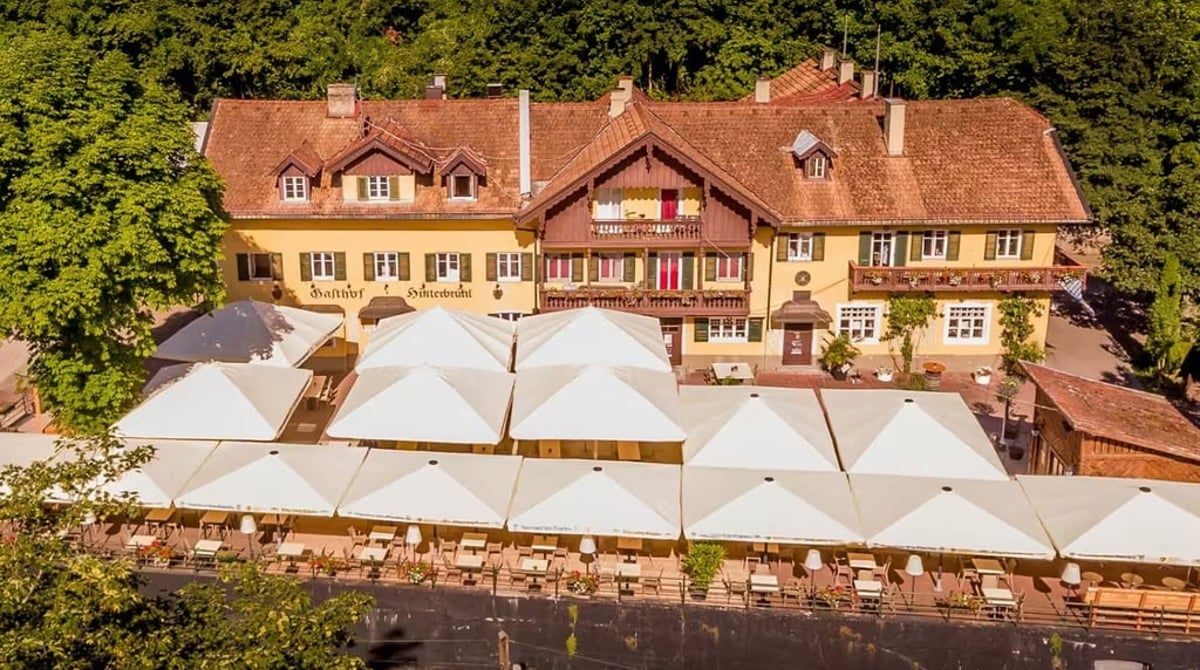 Luftaufnahme des Gasthofs Hinterbrühl mit Schirmen der Terrasse vor dem Wald