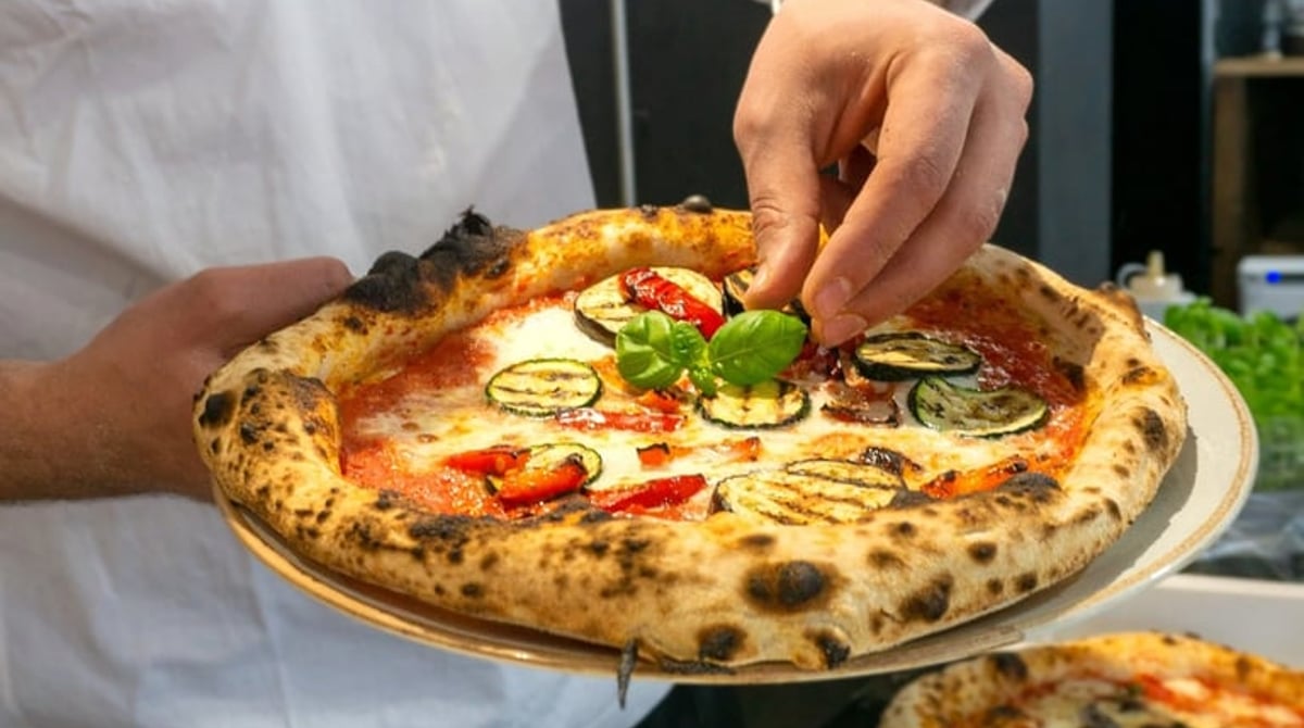 Pizzaiolo belegt eine Pizza mit gegrilltem Gemüse und Basilikum