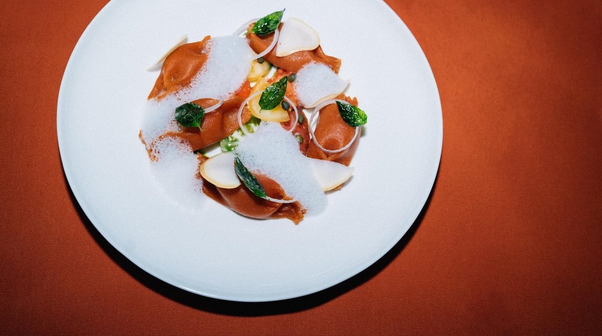 Ravioli mit Schaum und Kräutern auf einem orangefarbenen Untergrund