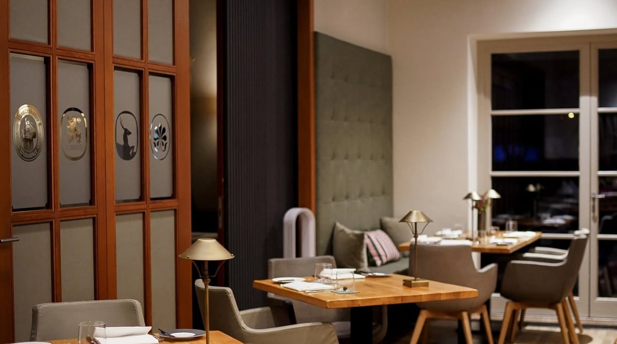 Gastraum des Restaurants 1804 mit gedeckten Holztischen, Polstersesseln und einer olivgrünen Polsterbank