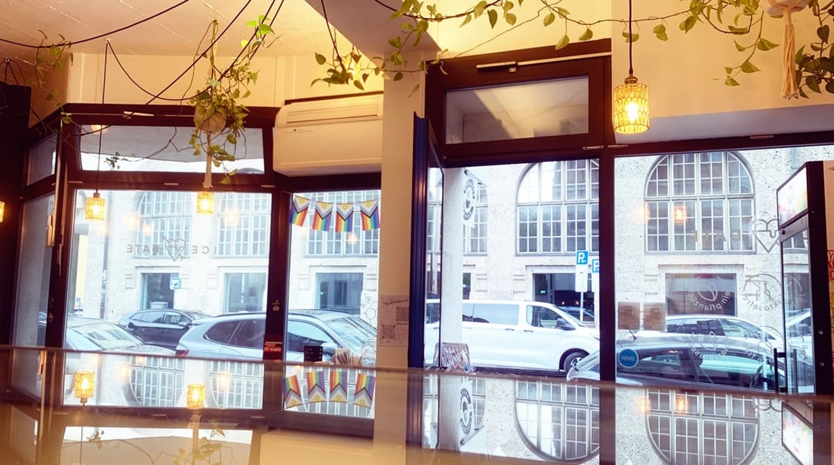 Café iceDate mit großen Fensterfronten, Hängelampen und Efeuranken, durch die Scheiben die Amalienstraße