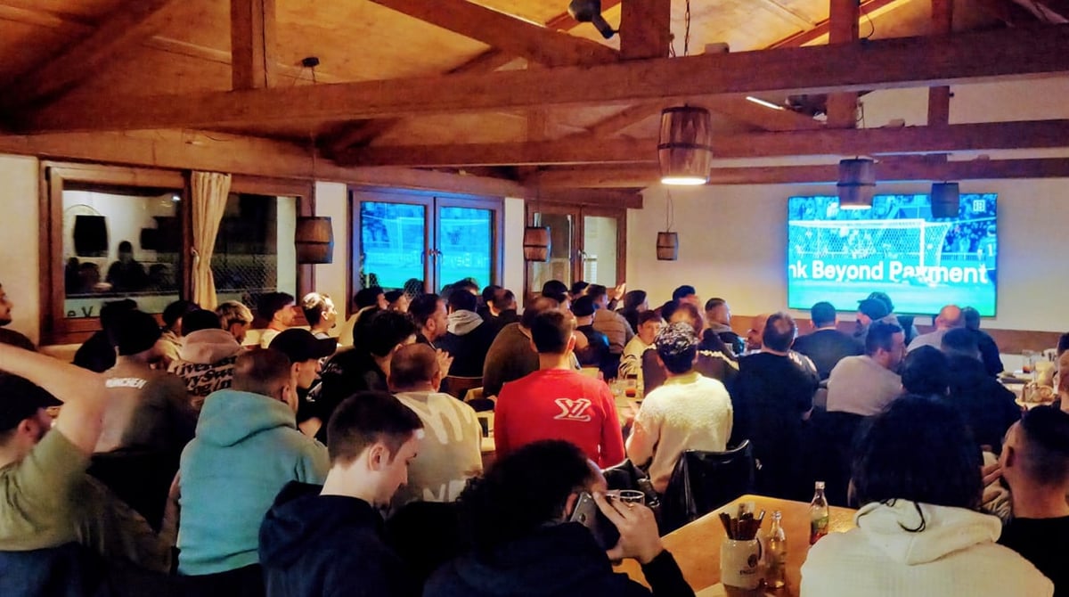 Gäste im Gastraum schauen gemeinsam Fußball auf einer großen Leinwand