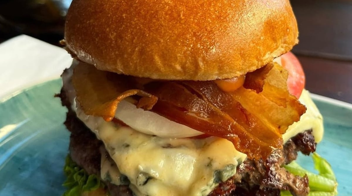 Burger mit Bacon und geschmolzenem Käse auf einem türkisfarbenen Teller