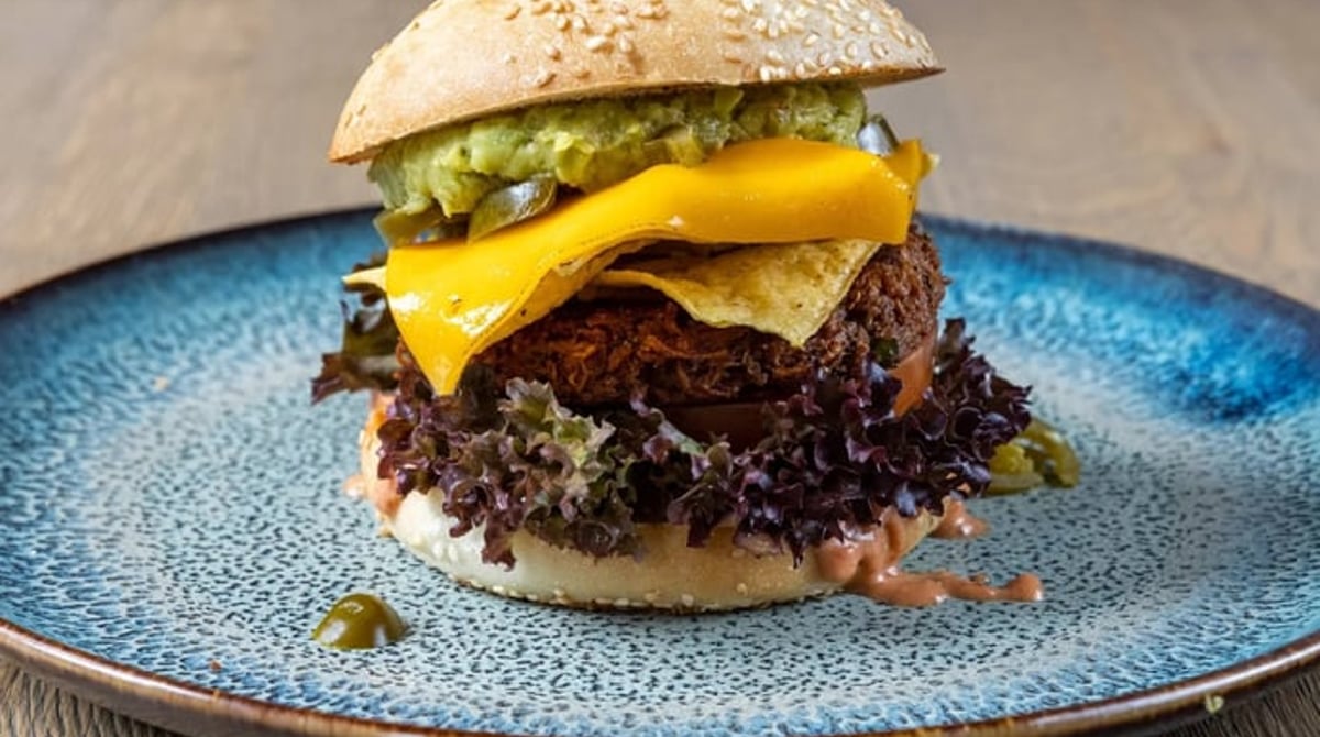 Burger mit Cheddar im Sesambrötchen auf einem blauen Teller