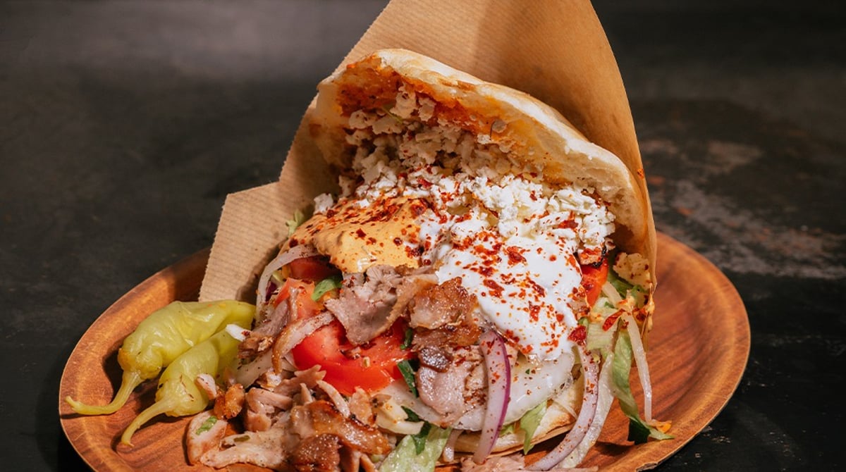 Döner mit Fleisch, Salat, Joghurtsauce und Peperoni auf einem Holzteller bei Django's
