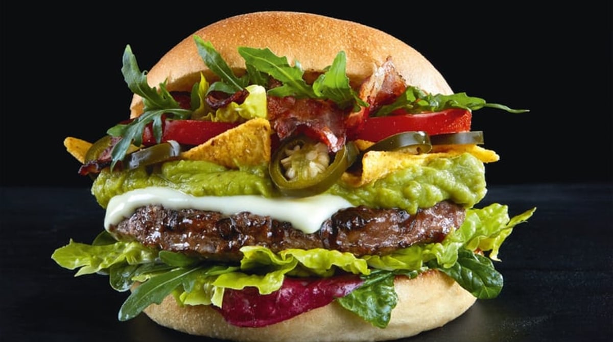 Burger mit Guacamole, Jalapeños, Tortillachips und Rucola vor dunklem Hintergrund