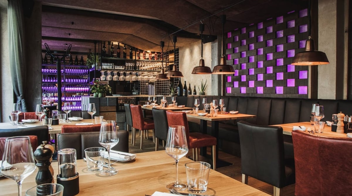 Gastraum des El Gaucho mit Holztischen, Ledersesseln und violett beleuchteter Wand