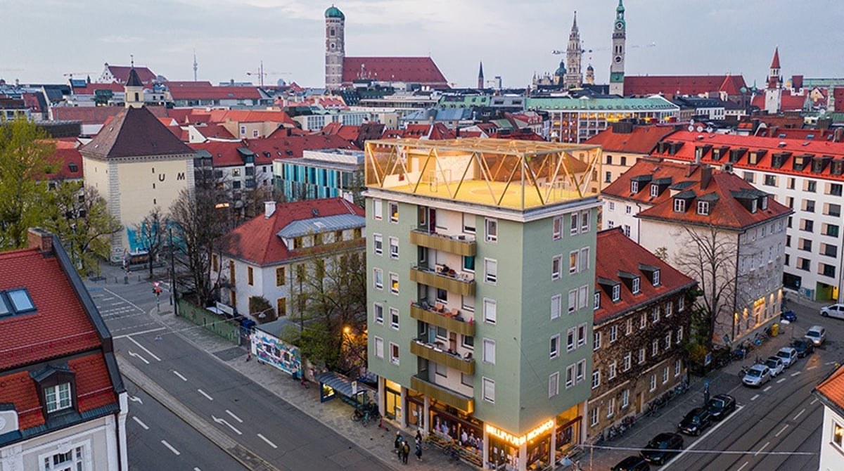Das Bellevue di Monaco an der Müllerstraße in der Abenddämmerung, Blick von oben auf das Haus mit Sportplatz auf dem Dach und die Dächer des Glockenbachviertels