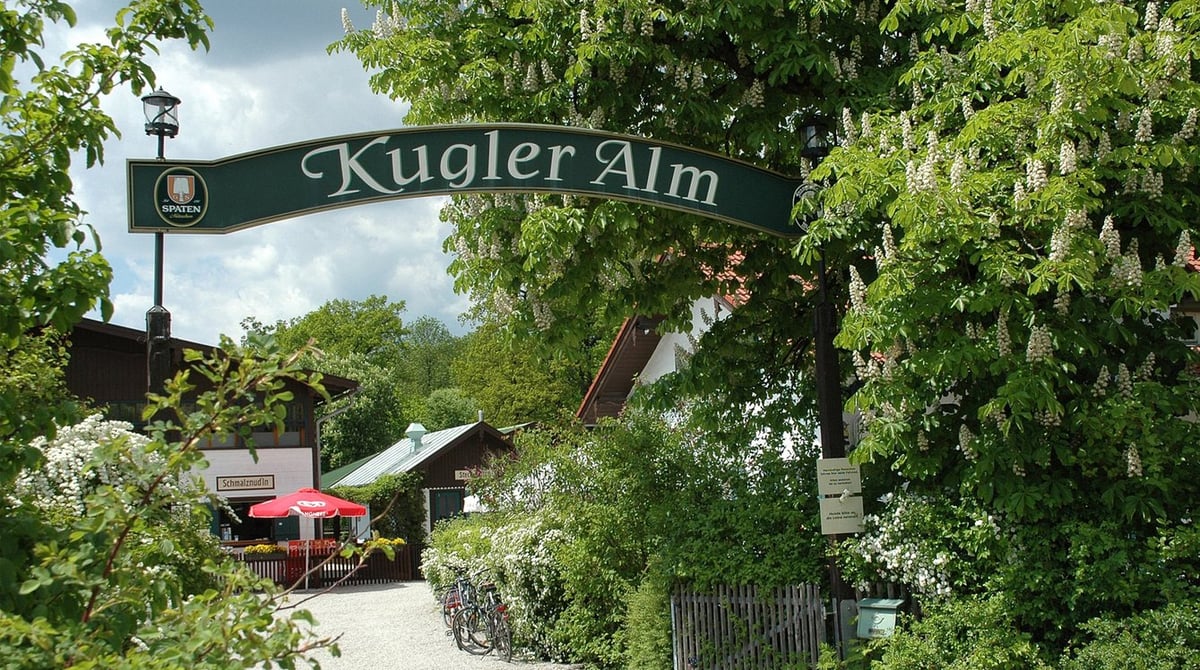 Eingang der Kugler Alm mit Holzschild unter blühenden Kastanien