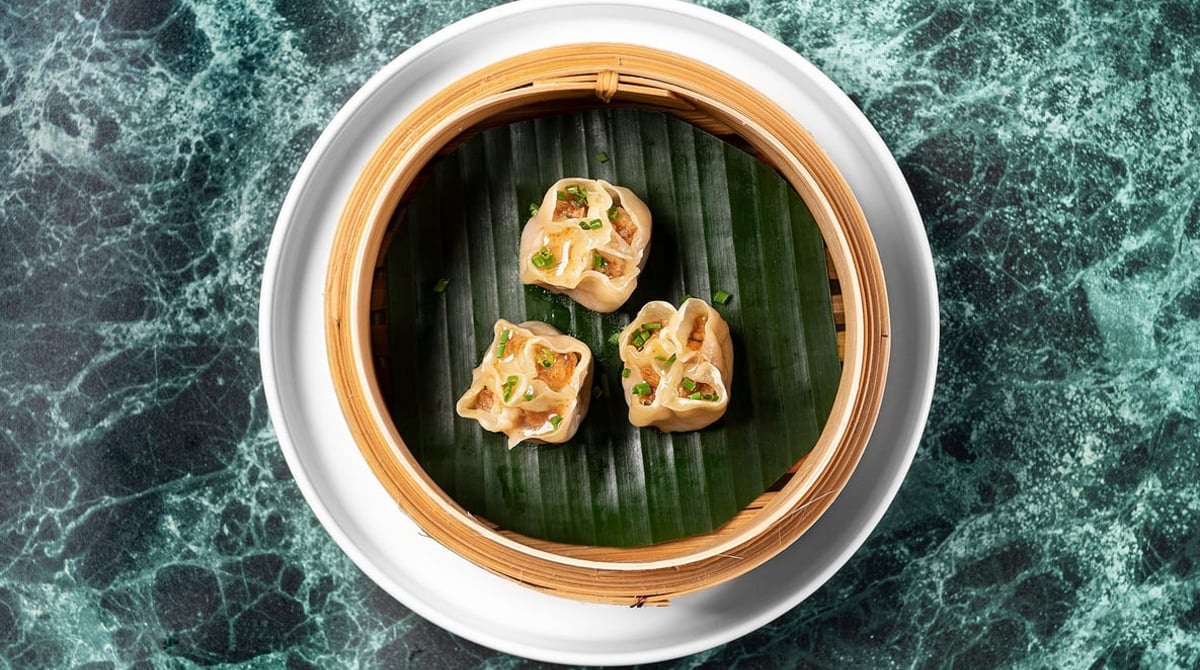 Dim Sum im Bambuskorb auf einem Bananenblatt vor grünem Marmor