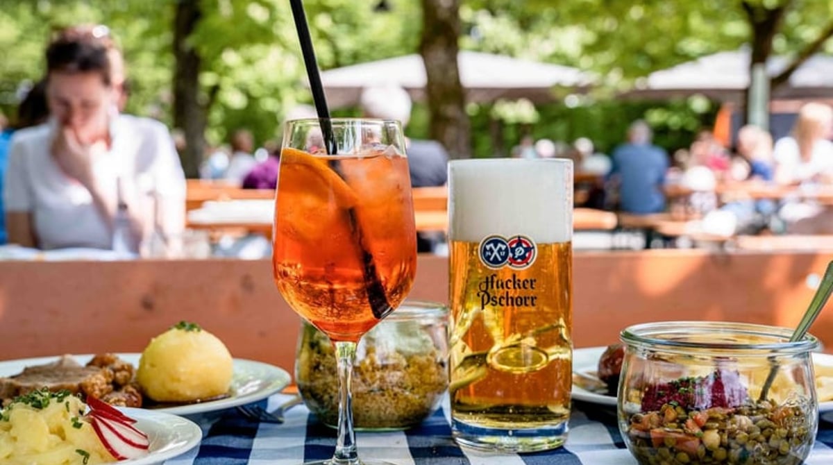 Bier, Spritz und Brotzeitgerichte auf einem karierten Biergartentisch