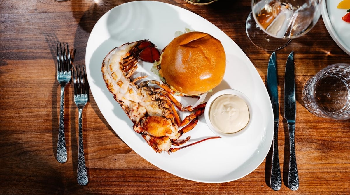 Halber gegrillter Hummer mit Cheeseburger und Lobster-Mayo auf einem weißen Teller