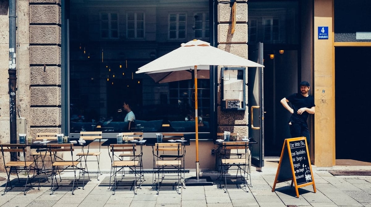 Eingang des kleinen Flo mit Schanigarten, Sonnenschirm und Kreidetafel an der Josephspitalstraße