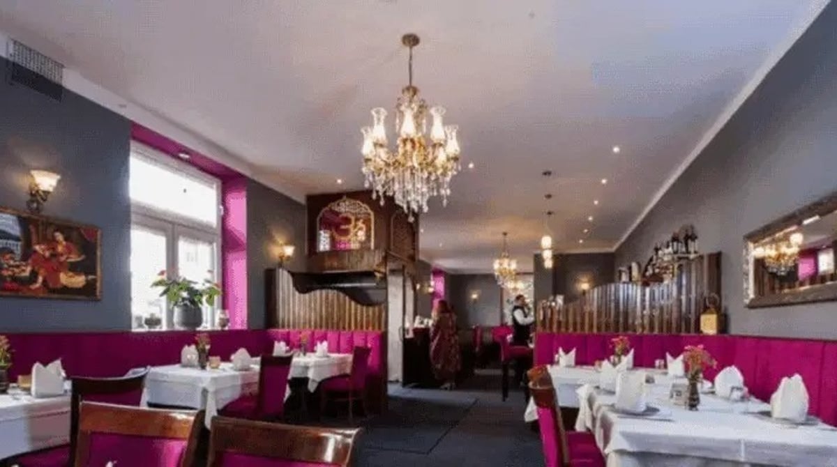 Gastraum des Royal India in München mit Kronleuchter, gedeckten Tischen und pinkfarbenen Sitzbänken