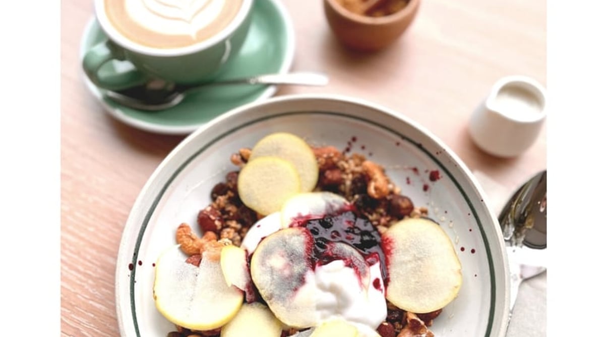 Latte mit Latte Art und eine Frühstücksschale mit Apfelscheiben, Nüssen und Joghurt