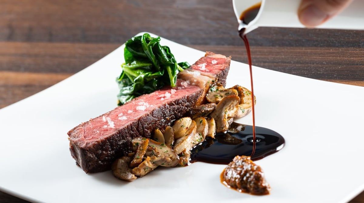 Rinderfilet in Scheiben mit Pilzen und Mangold, daneben wird dunkle Sauce angegossen