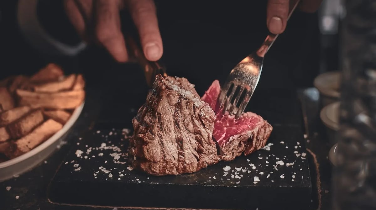 Steak wird auf einem heißen Stein mit Meersalz geschnitten, daneben Pommes auf einem Teller