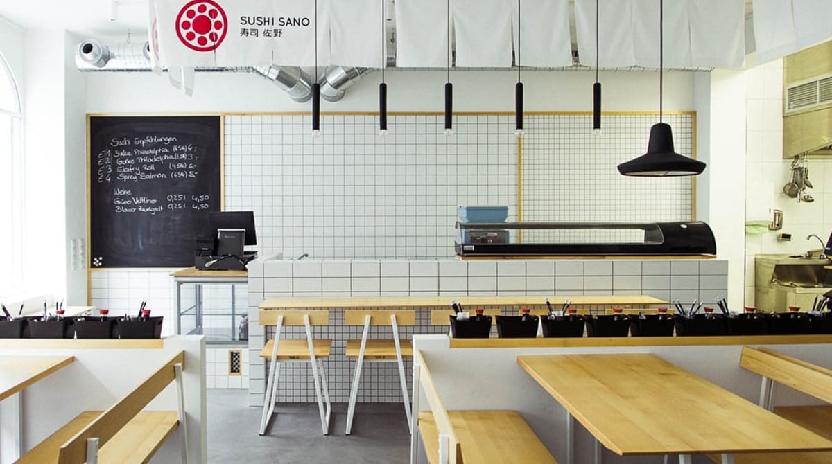 Heller Gastraum des Sushi Sano mit Holztischen, Bänken, Sushi-Theke und Kreidetafel an der Zweibrückenstraße