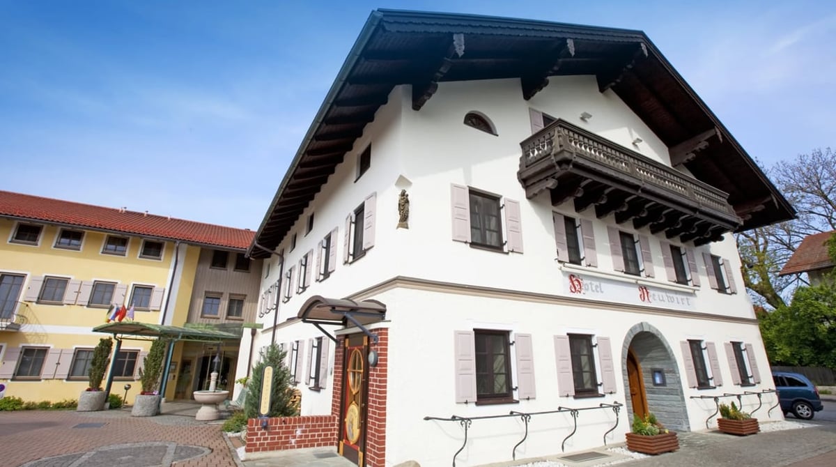 Das weiße Haus des Hotels Neuwirt in Sauerlach mit Satteldach und Holzbalkon vor blauem Himmel