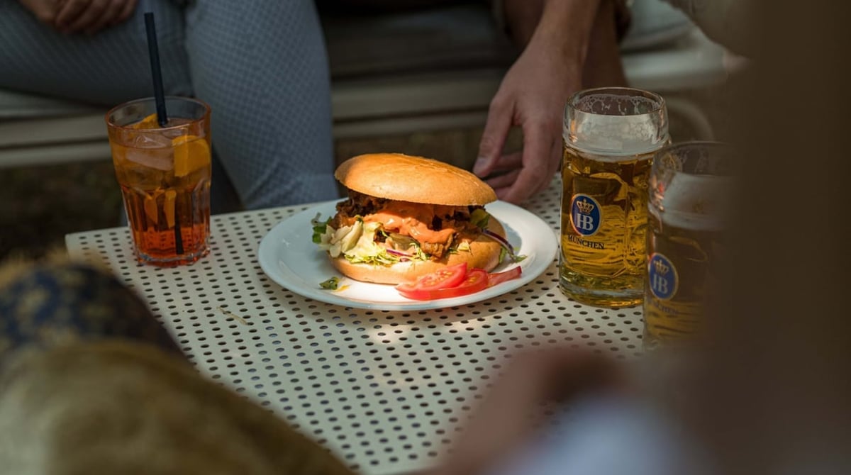 Belegte Semmel mit Hofbräu-Maß und Aperitif auf einem Gartentisch