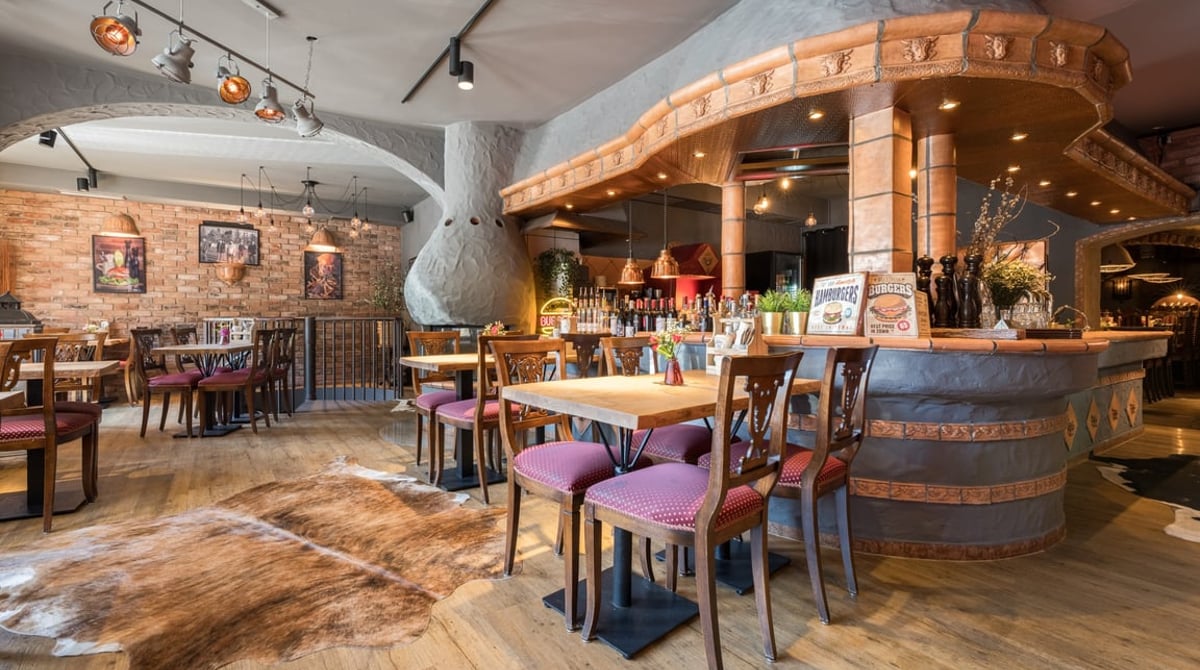 Gastraum der Pablo Emilio BurgerBar in Planegg mit Gewölbedecke, Ziegelwand, Holztheke und eingedeckten Tischen