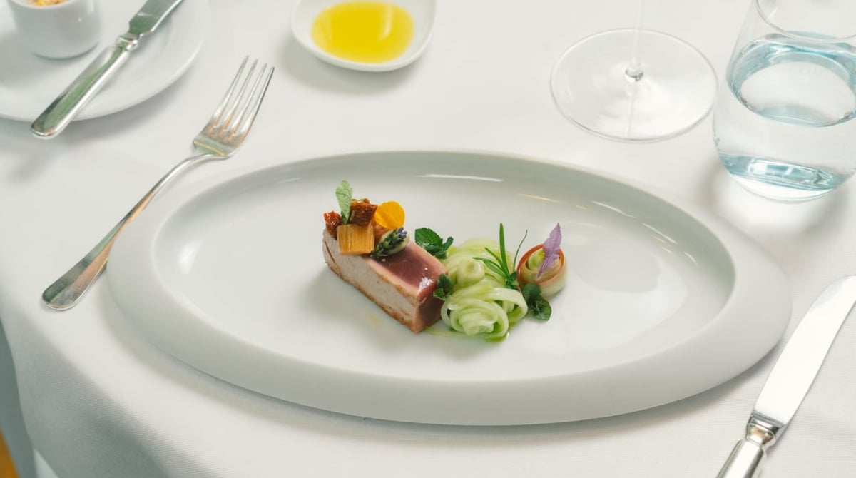 Kleine Vorspeise auf einem ovalen weißen Teller an einem gedeckten Tisch mit Besteck und Olivenöl