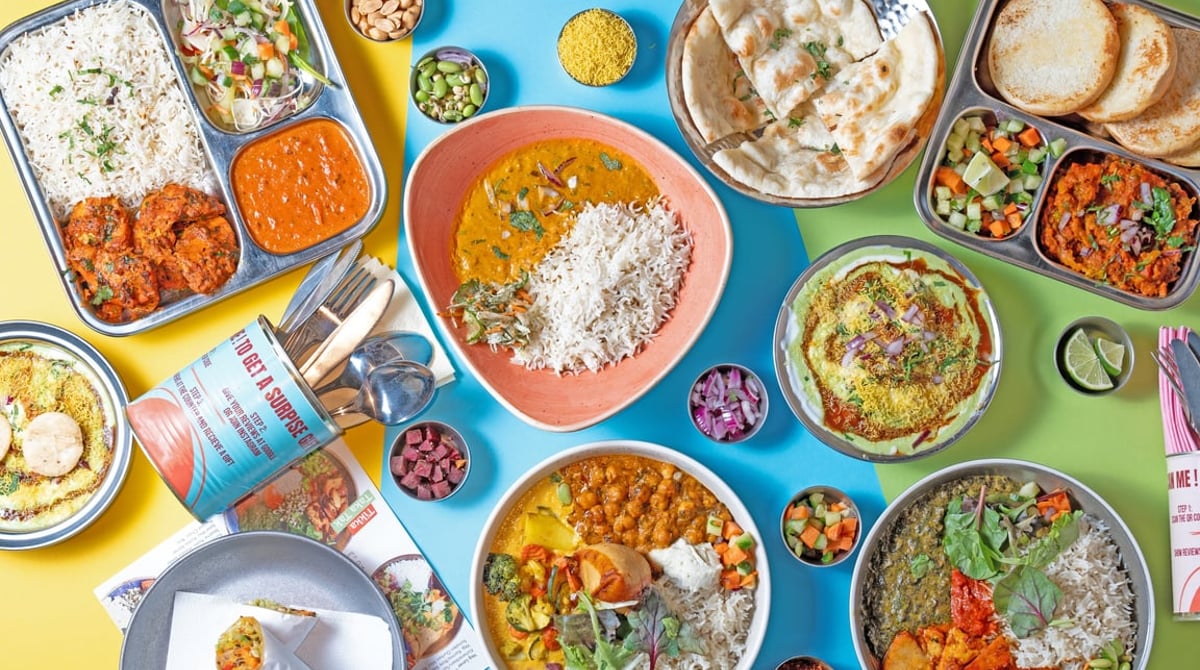 Bunte Tafel mit Currys, Thali-Tellern und Naan auf farbigem Grund
