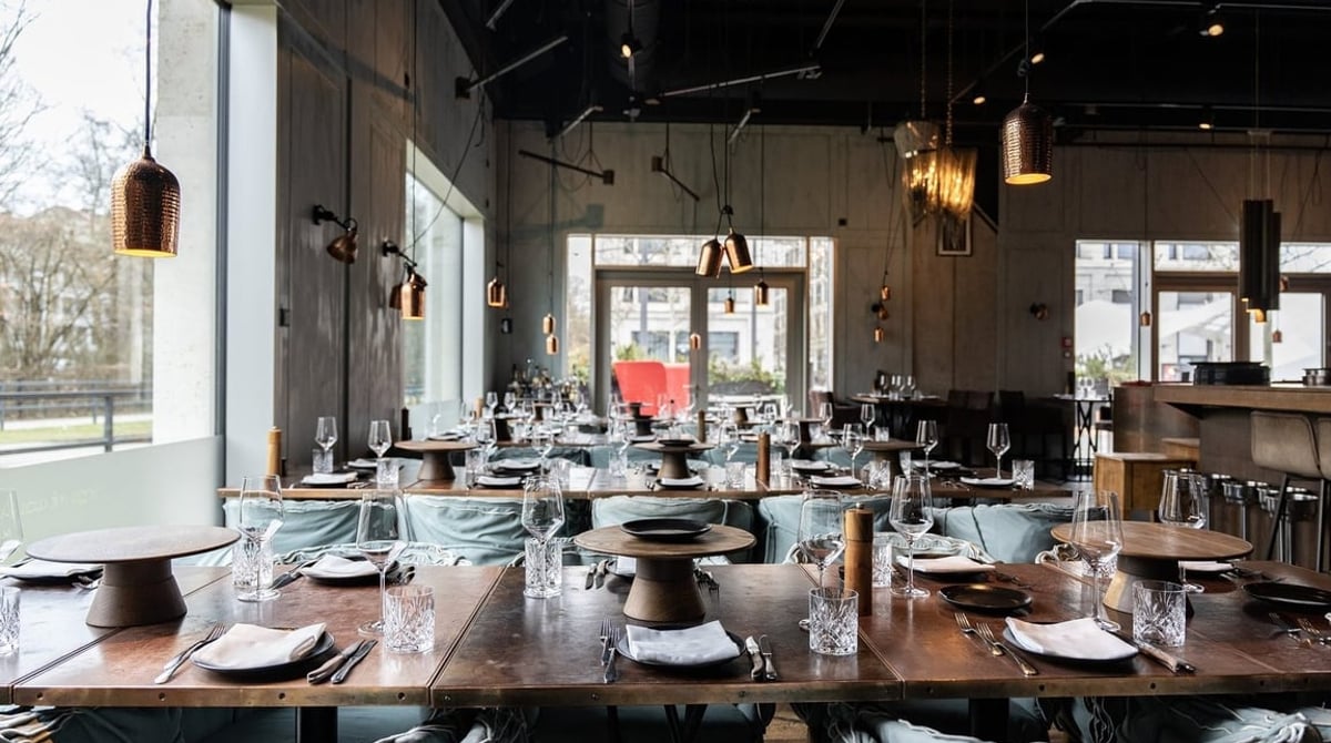 Gastraum des La Bohème mit gedeckten Holztischen und großen Fenstern
