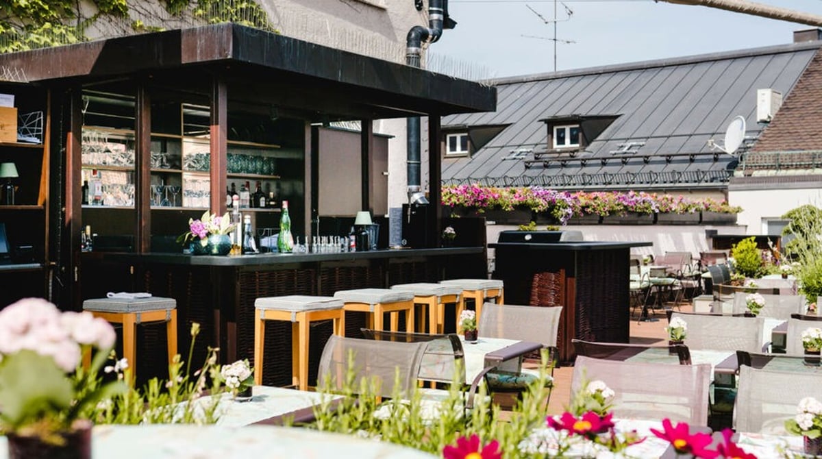 Die Dachterrasse des LOUIS Hotels mit Bar, Sitzplätzen und Blumen