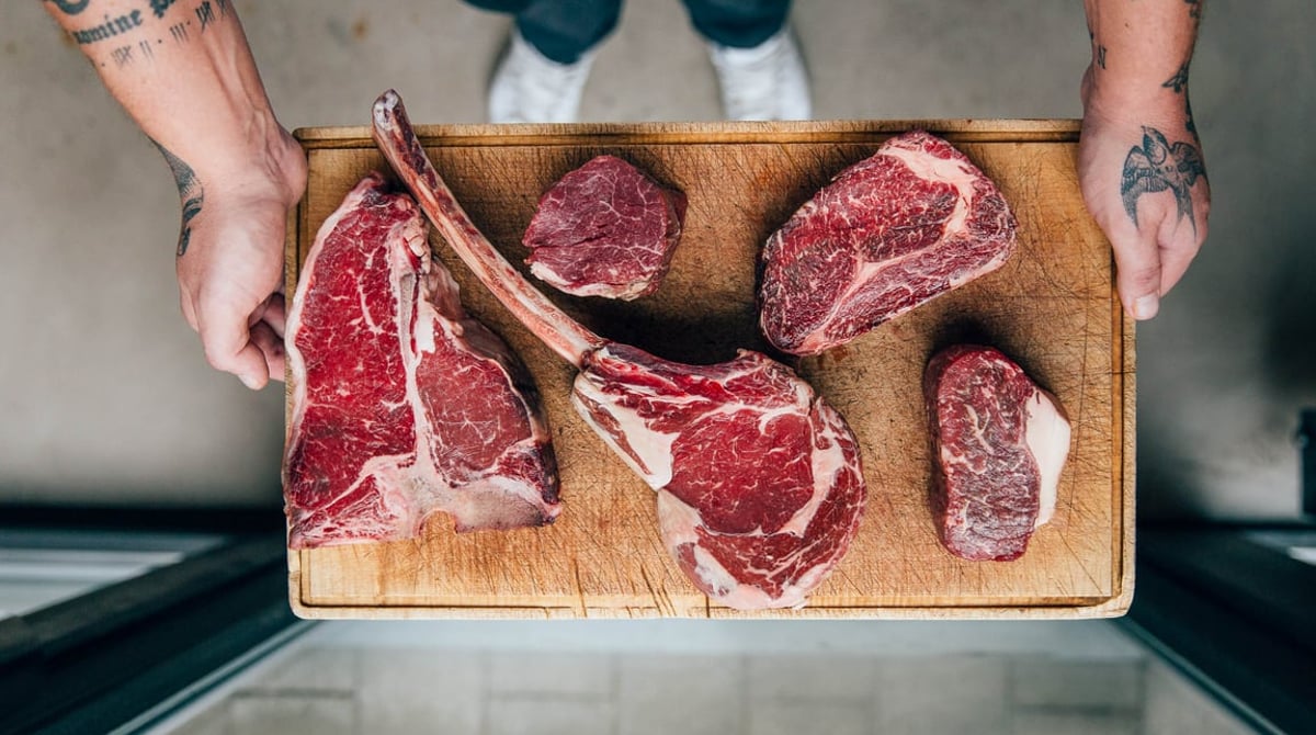 Köche mit einem Holzbrett voller roher Cuts, darunter ein Tomahawk-Steak