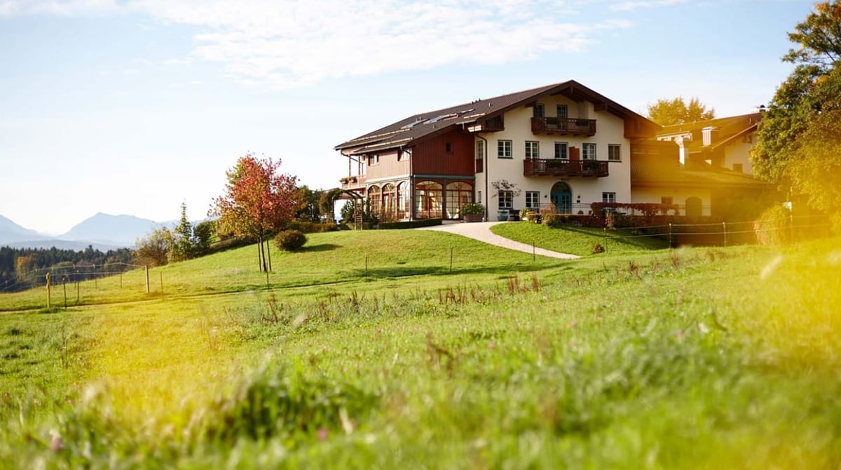 Der Aschbacher Hof auf der Anhöhe bei Feldkirchen-Westerham mit Wiese und Bergen im Hintergrund