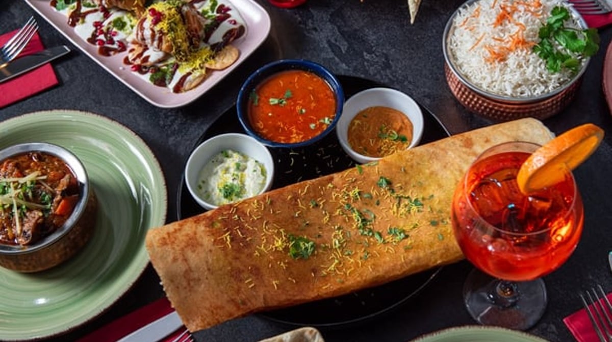 Gedeckter Tisch mit Dosa, Naan, Currys, Reis und Getränken